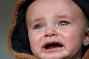 Parent calmly sitting beside a screaming toddler in a messy bedroom